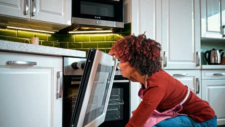 A woman crouching to look into an oven in a bright kitchen